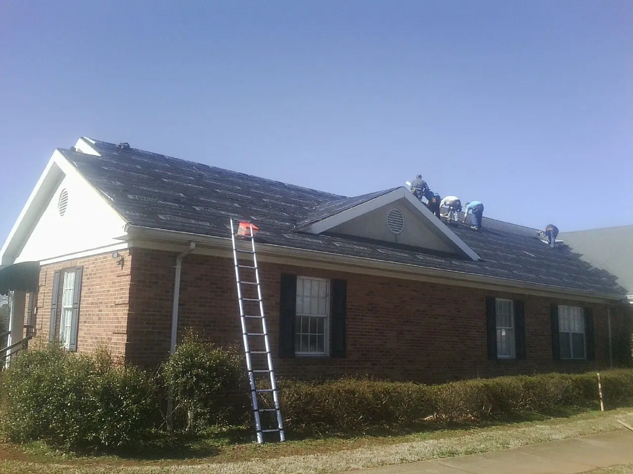 Crew tearing shingles off a brick ranch roof with a ladder set — Metal Roof Repair work by our crew in Littleton