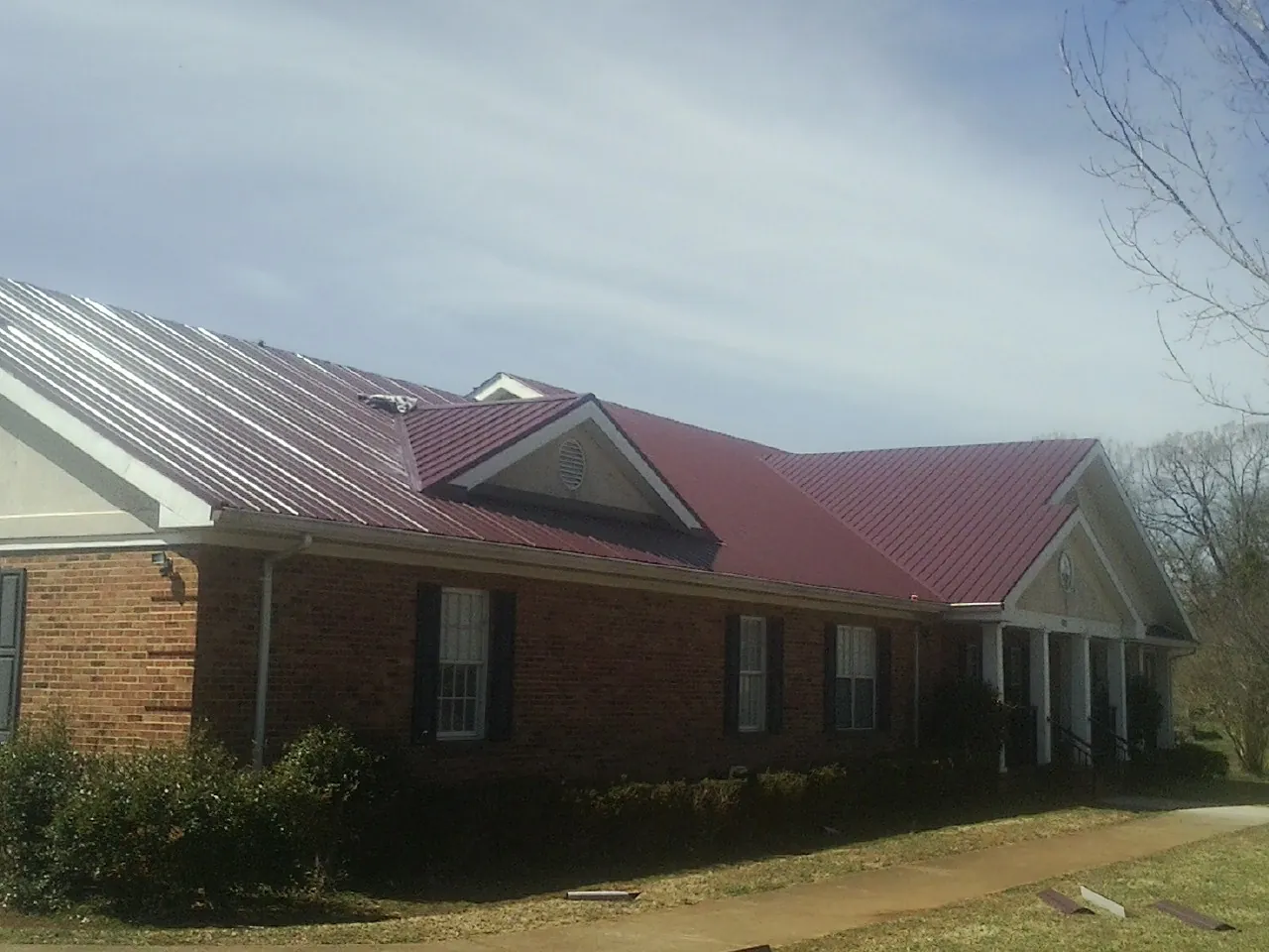 Red metal roof with gabled entries on a long brick building, from a Hail Damage Roof Repair job in Littleton