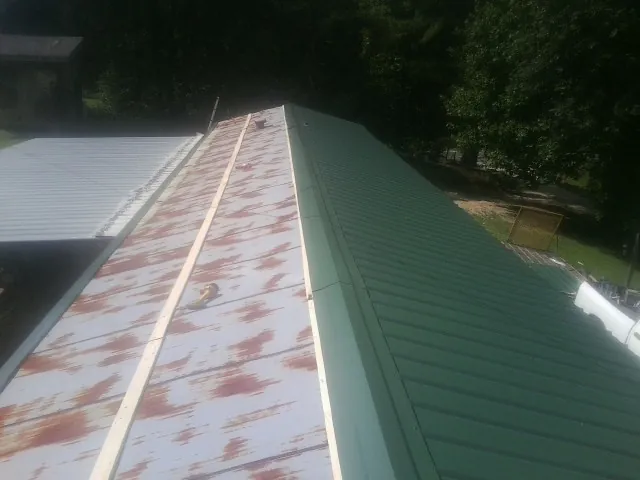 Old rusted panels beside newly installed green metal roofing — Wind Damage Roof Repair by Roofing Brothers in Littleton